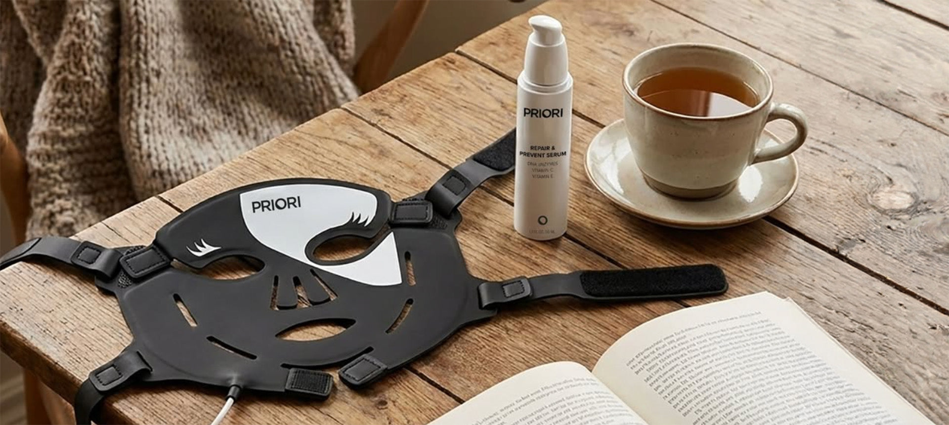 PRIORI red light face therapy mask for elevated skincare on a coffee table with face serum, a cup of tea, and a good book 