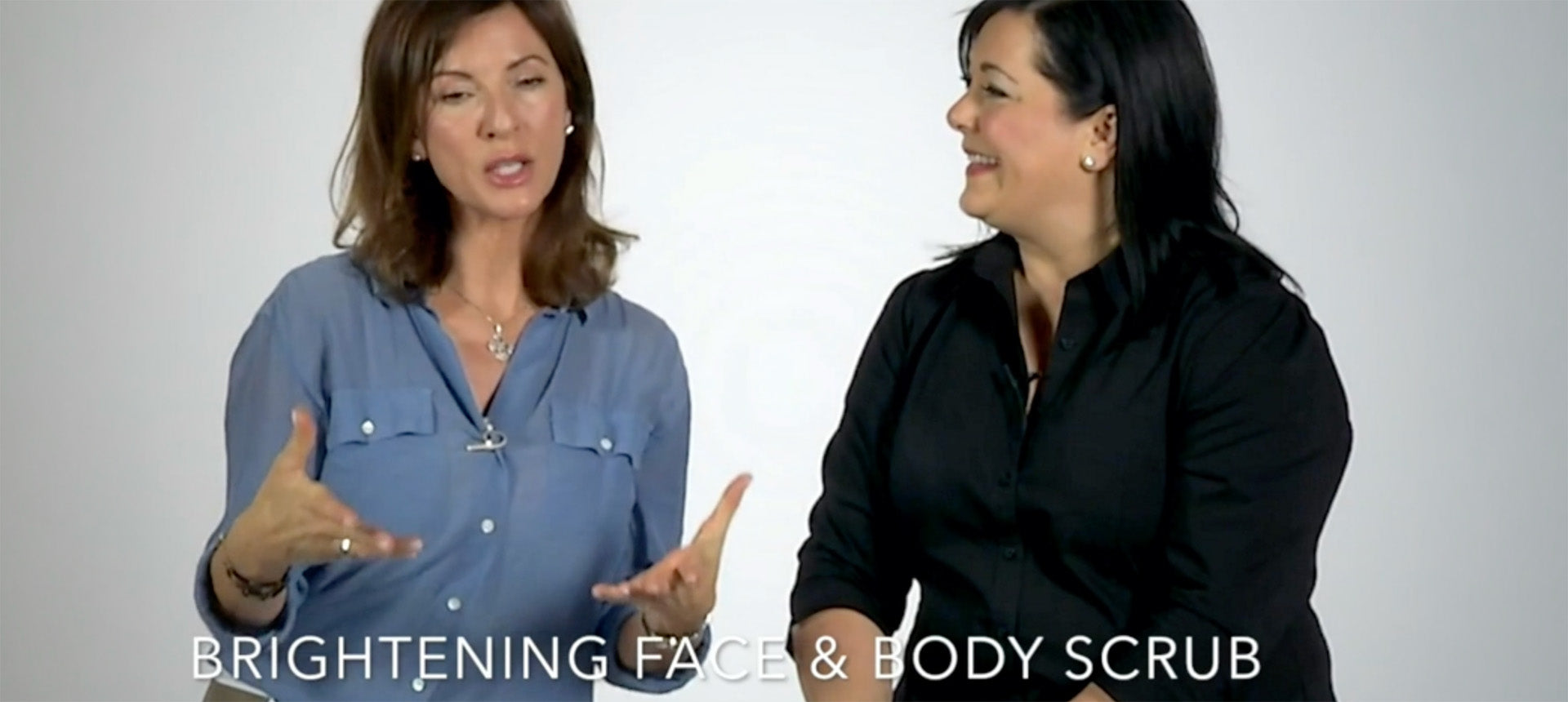 Two women discussing a PRIORI brightening face & body scrub with natural chemical peel against a plain background